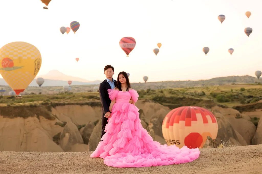 Couple posing for a pre-wedding photoshoot in Cappadocia with hot air balloons at sunrise
