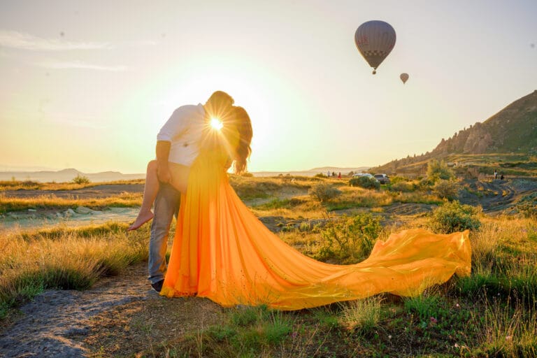 Romantic couple kissing at sunset in Cappadocia with hot air balloons