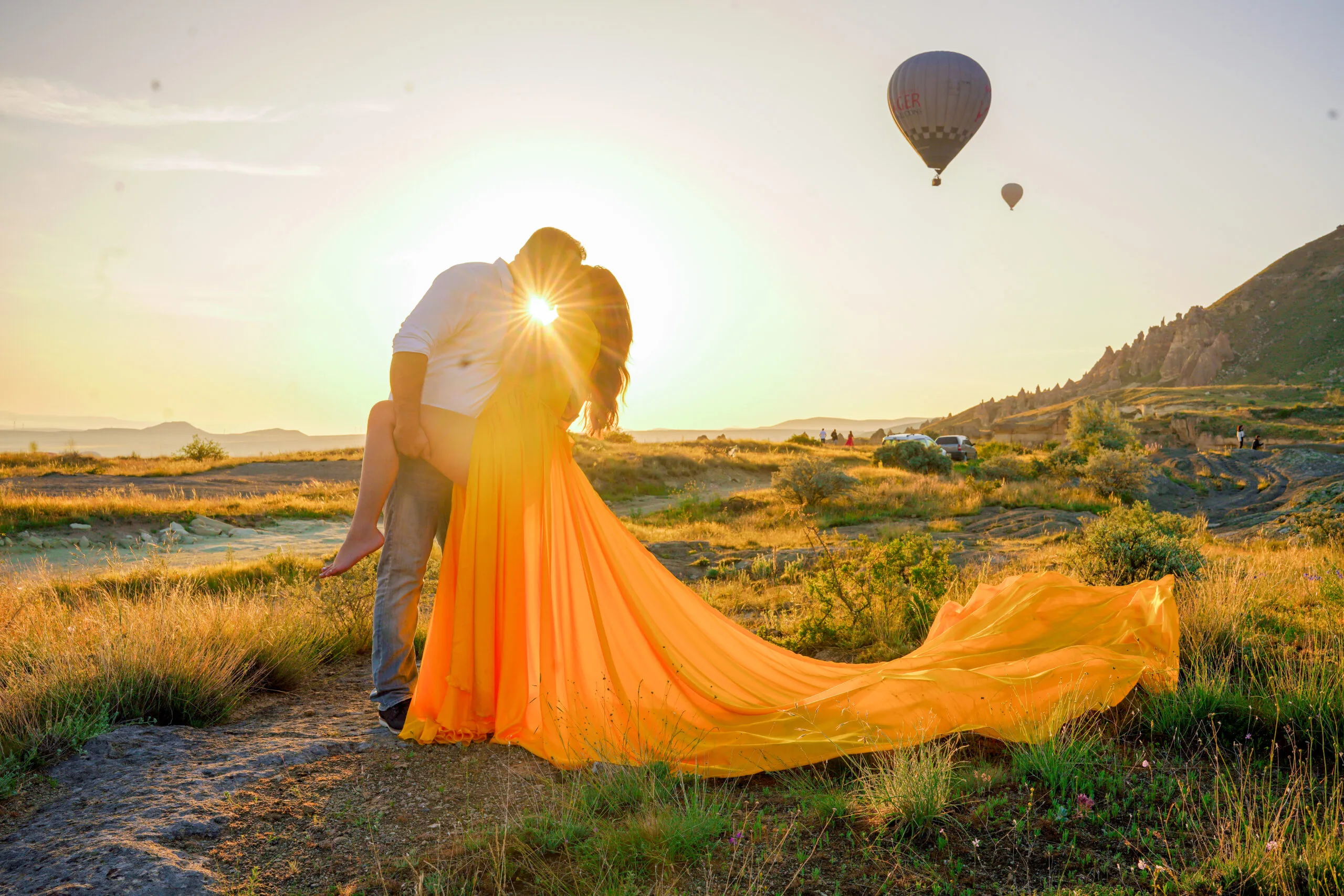 Romantic couple kissing at sunset in Cappadocia with hot air balloons