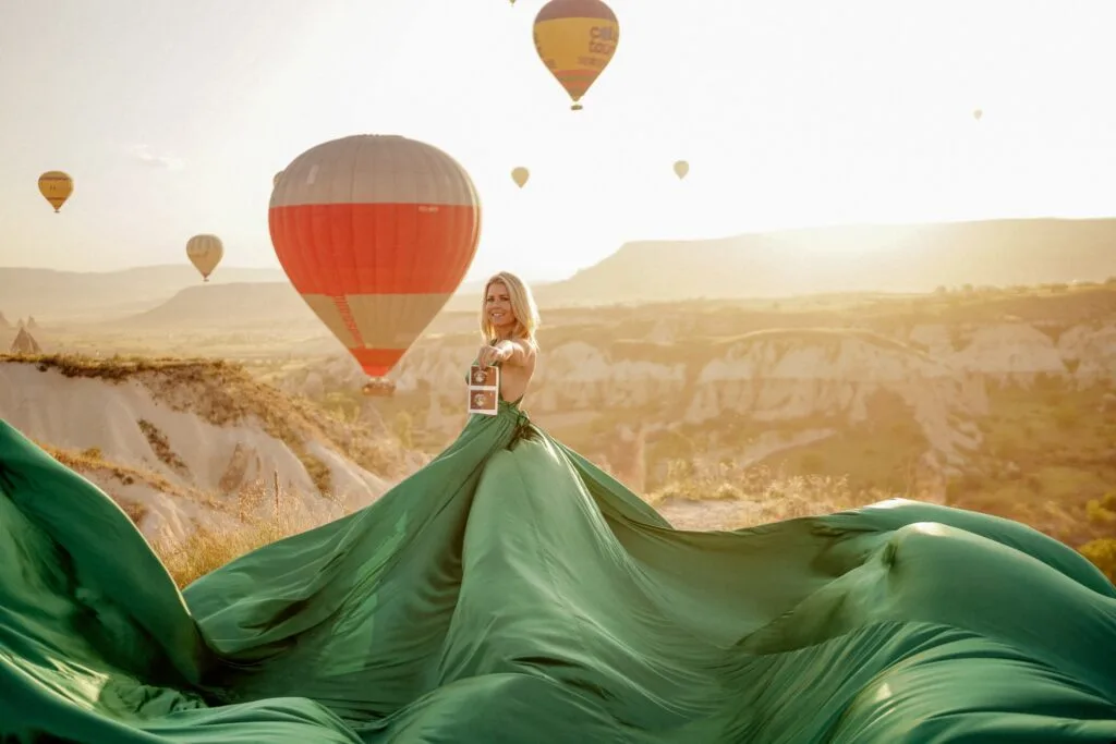 Pregnant woman in a green dress with hot air balloons in Cappadocia