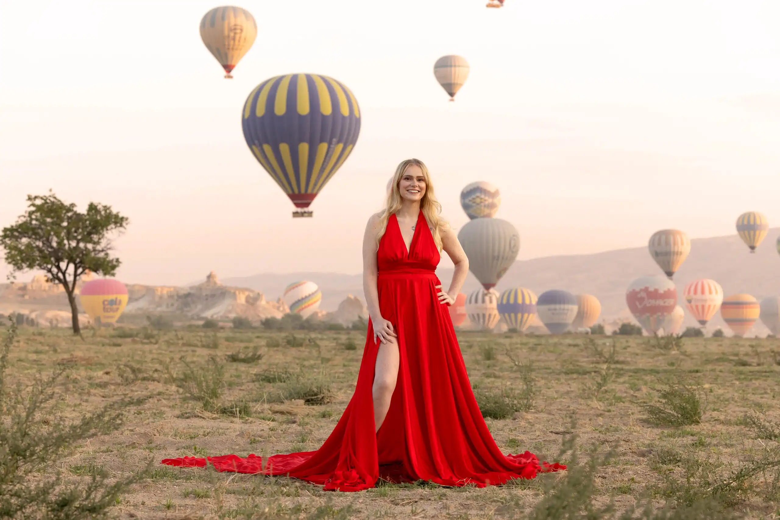 Woman in a red dress posing in front of hot air balloons at sunrise in Cappadocia