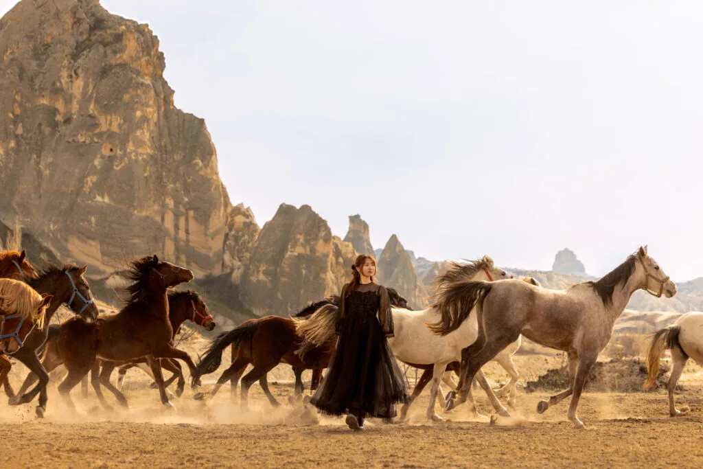 Black dress woman walking among running horses in Cappadocia
