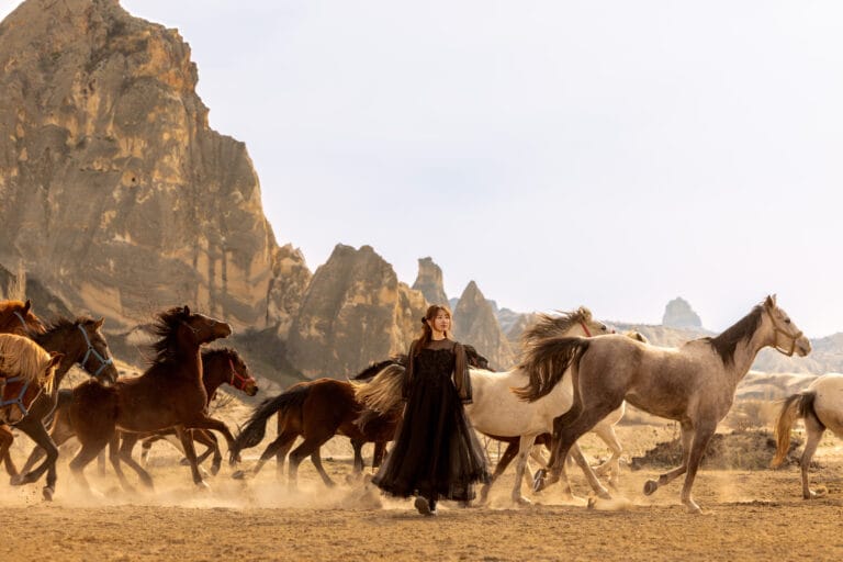 Black dress woman walking among running horses in Cappadocia